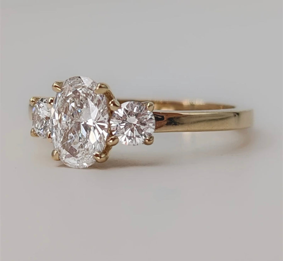 An oval ice cut Moissanite ring with two round side moissanites set in a yellow gold band.