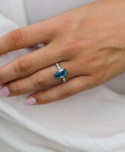 A hand displaying a pear-cut crushed ice Moissanite ring with a hidden halo design, set in a band possibly made of silver or gold.