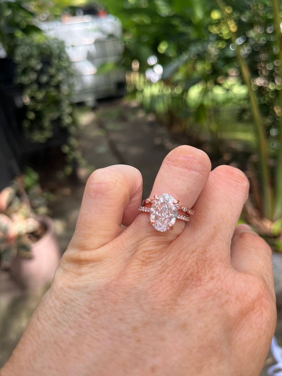 A hand displaying a bridal ring set, with the main ring featuring a crushed ice Moissanite stone, and a dainty marquise wedding band.