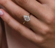 A hand displaying a 3ct pear cut Moissanite ring on a finger, with the ring's enclosure visible.