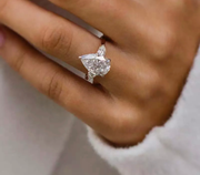 A hand holding a crushed ice hybrid pear cut Moissanite ring with a silver band and a VVS1 clarity diamond.