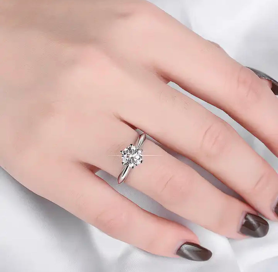 A woman's hand displaying a 1ct round solitaire Moissanite ring on her finger.