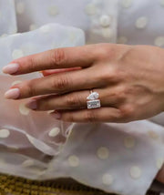 A woman's hand displaying a diamond ring with a silver band, set on a polka-dotted background.