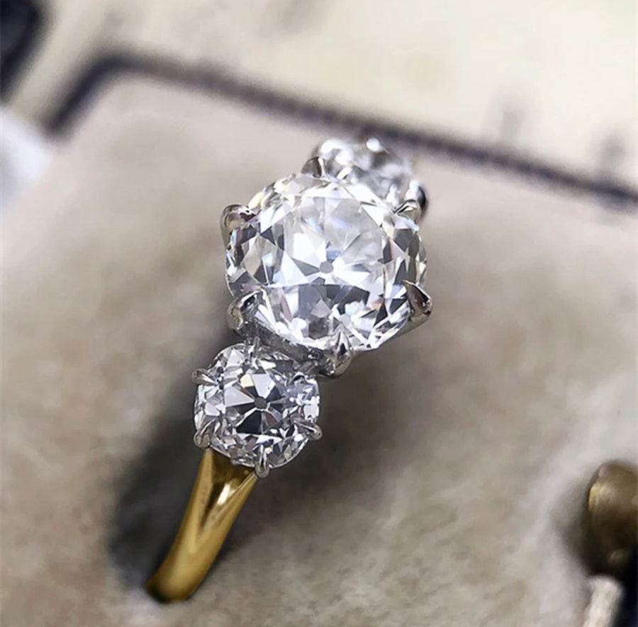 A three-stone Moissanite diamond ring with a central 2ct stone and two 1ct stones, set in a gold band.