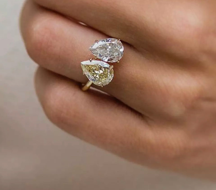 A hand holding a two-tone pear shaped yellow and white Moissanite ring with white gold plating.